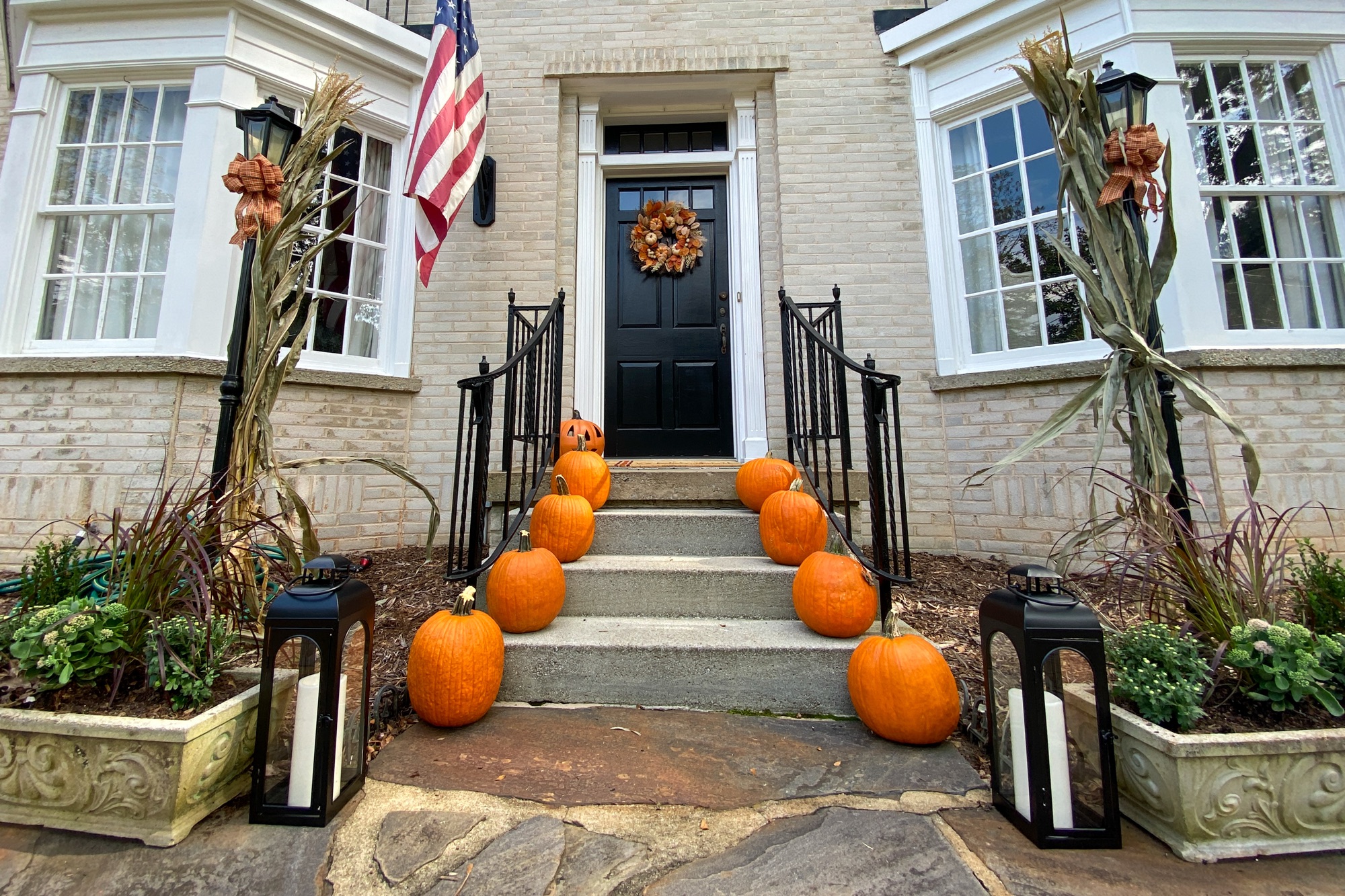 Fall porch with pumpkins, lanterns, cornstalks, and a wreath — an inviting seasonal entryway idea.