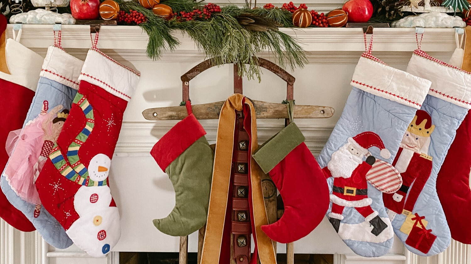 Christmas stockings hanging on a decorated mantel with greenery, bells, and handmade holiday details in a cozy home setting.