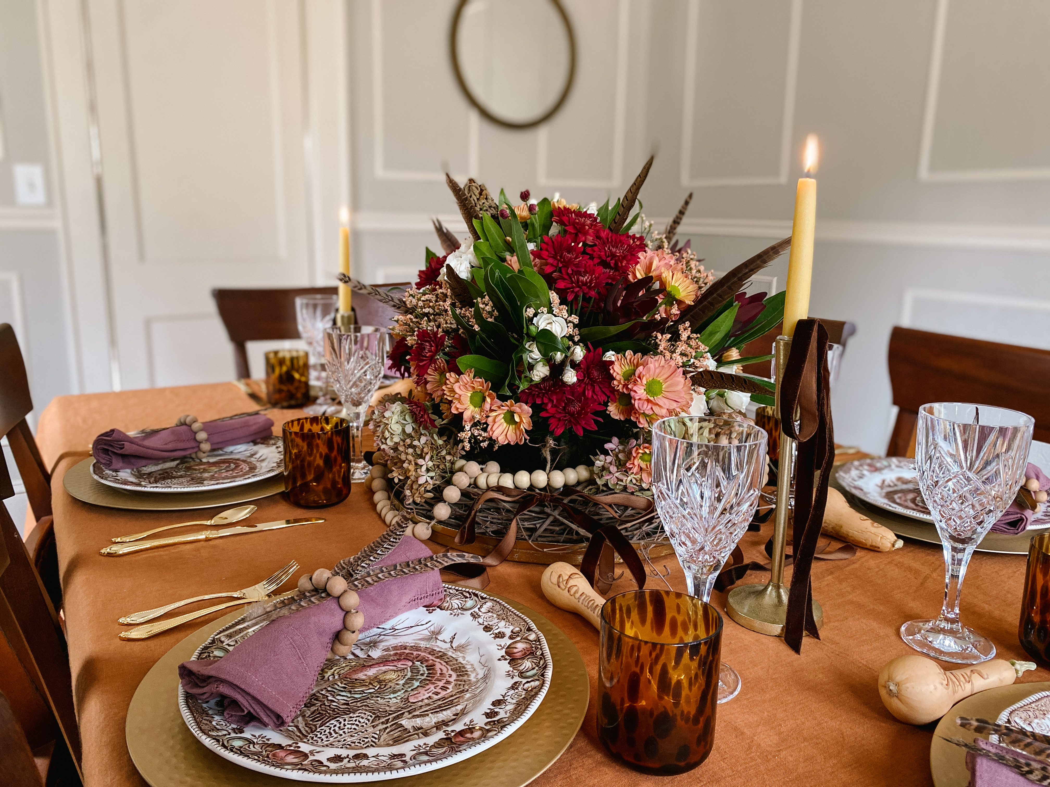 Vintage Thanksgiving table with turkey plates, fall flowers, and amber glassware on a rust-colored tablecloth.