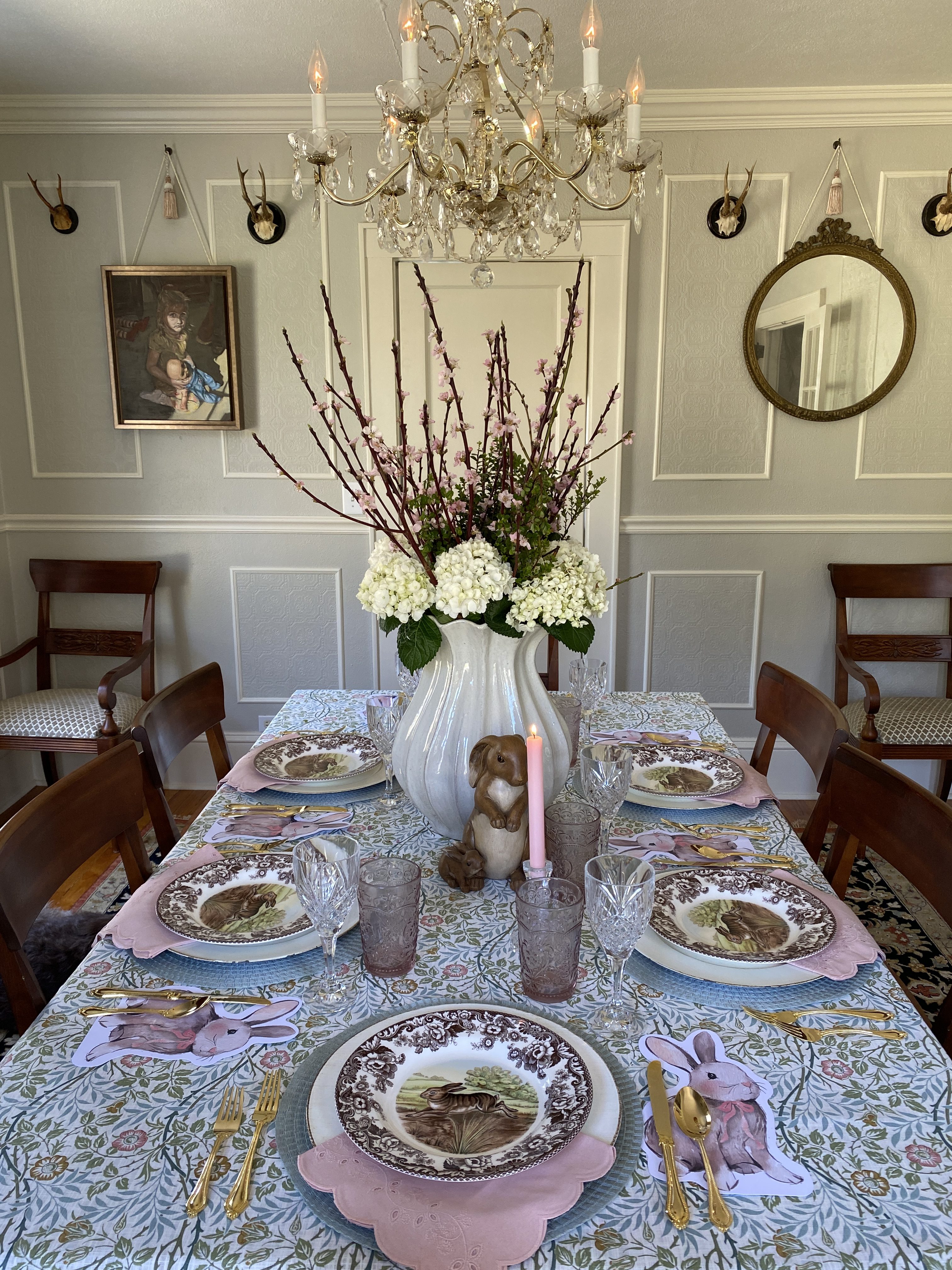 Classic spring easter table setting with layered vintage and new tableware, pink linens, crystal glassware, and floral centerpiece