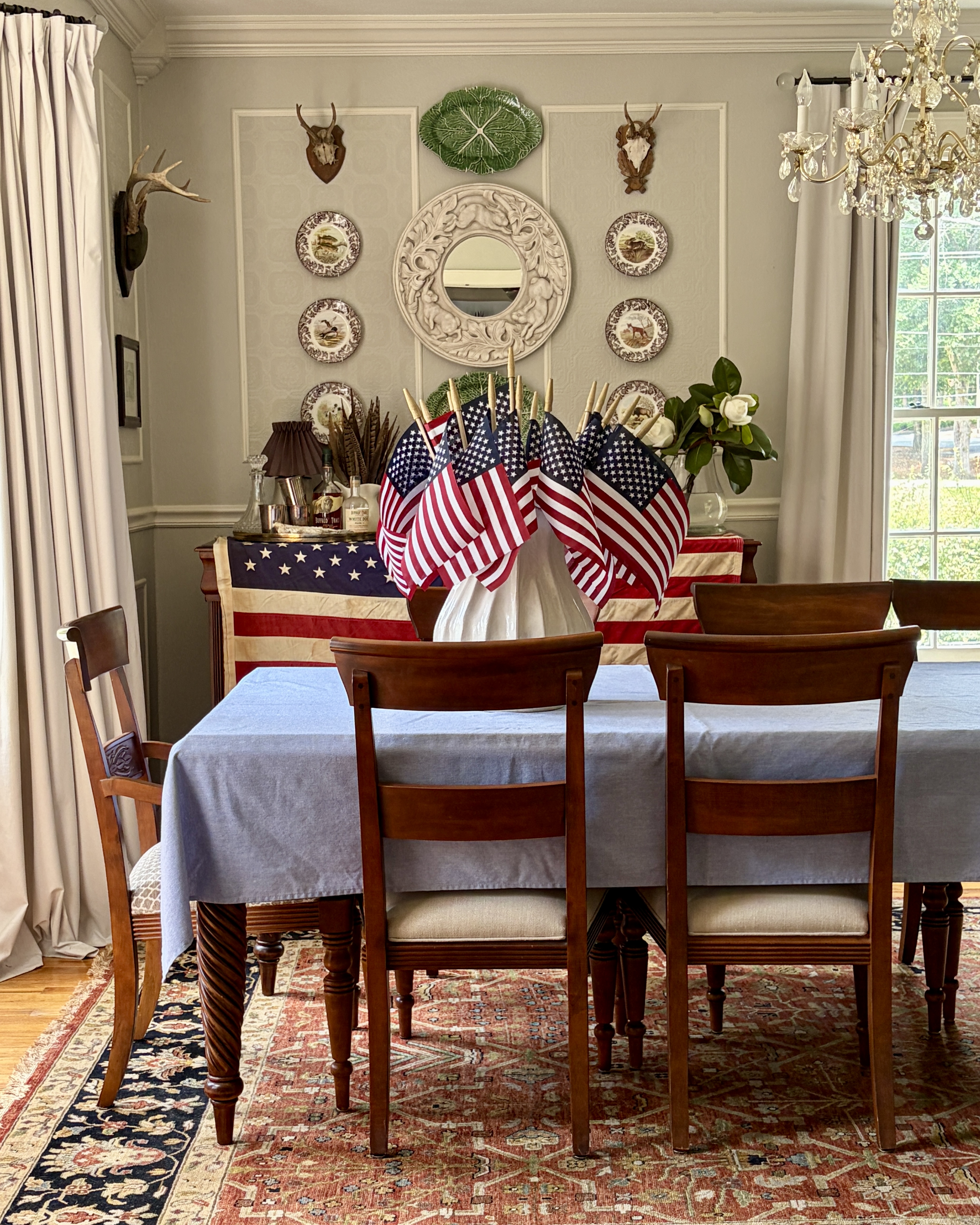 Southern dining room decorated in Americana style with traditional furnishings, layered textiles, vintage flags, and collected antiques
