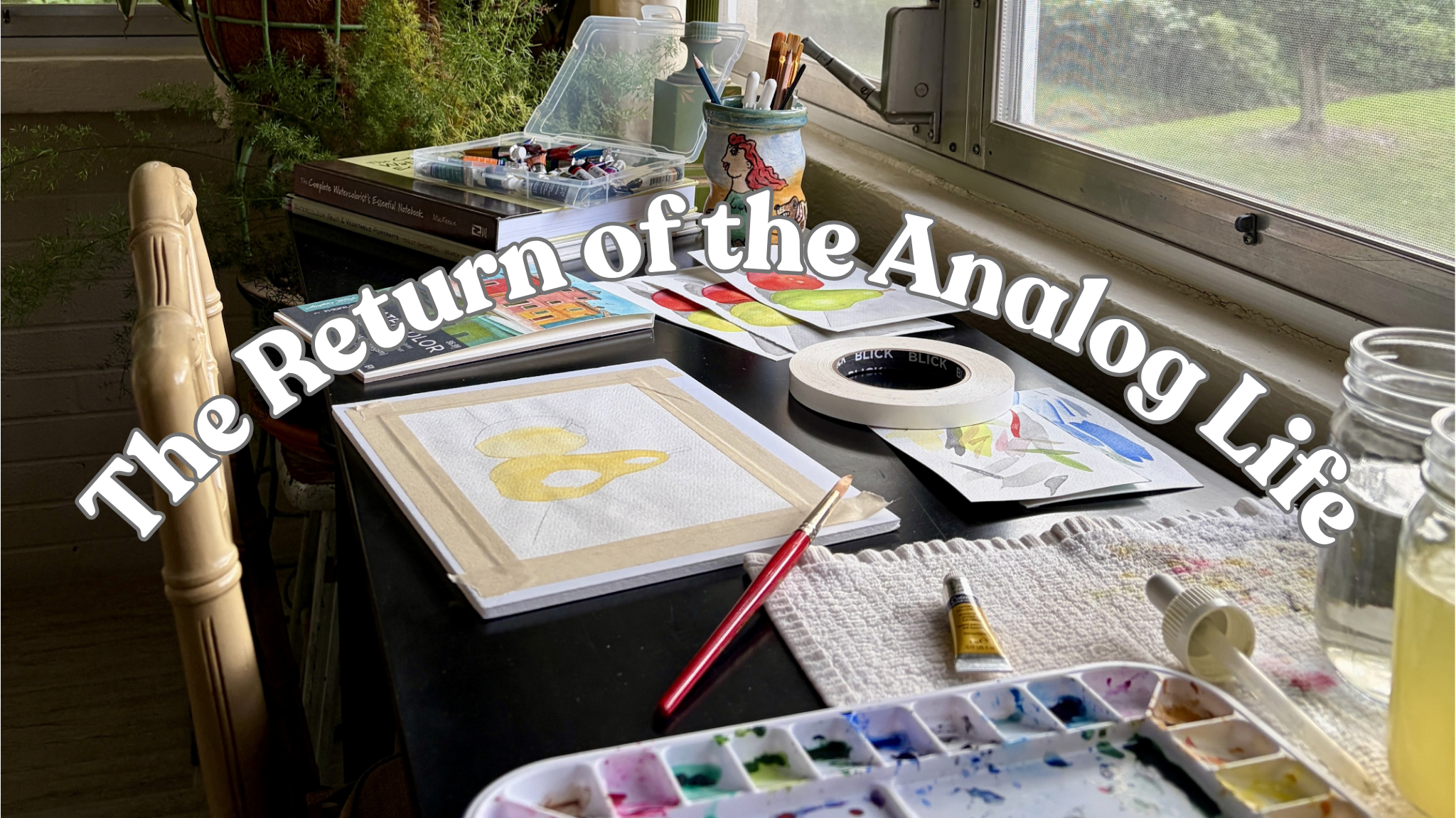 Watercolor paintings in progress with brushes, books, and art supplies beside a window.